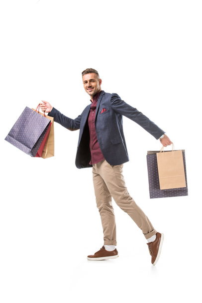 sonriente adulto hombre shoppper en chaqueta caminar con colorido papel bolsas aislado en blanco
 - Foto, Imagen