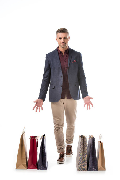 alegre hombre con estilo en la chaqueta que apunta a las bolsas de compras de colores aislados en blanco
 - Foto, Imagen