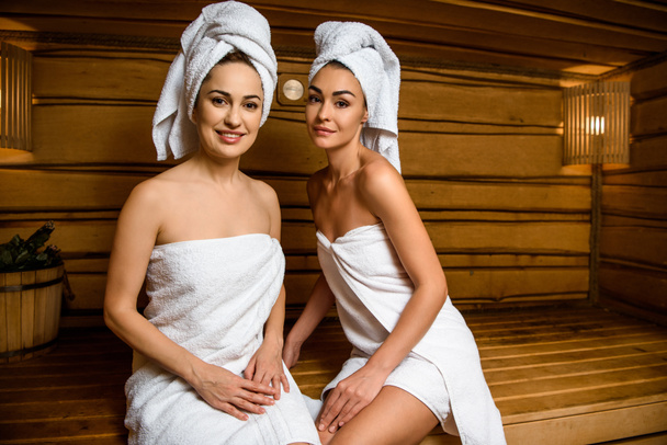 beautiful young women sitting together in sauna and smiling at camera  - Fotoğraf, Görsel