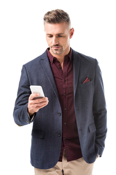 focused adult stylish man in jacket using smartphone isolated on white - Zdjęcie, obraz