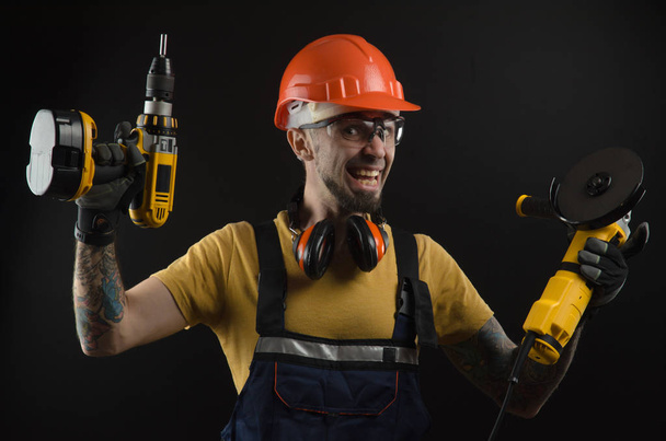 un giovane uomo in posa su uno sfondo nero in uniforme da lavoro e uno strumento di costruzione
 - Foto, immagini