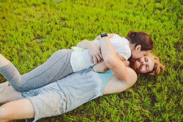 スポーツと健康的なライフ スタイル テーマです。若い男性と女性のカップルは、スポーツをプレイした後緑の草に背、パックで芝生の上に横たわって休んでいます。家族の合同訓練. - 写真・画像