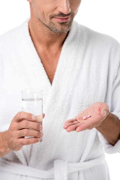 partial view of adult man in bathrobe holding pills and glass of water isolated on white - Photo, image