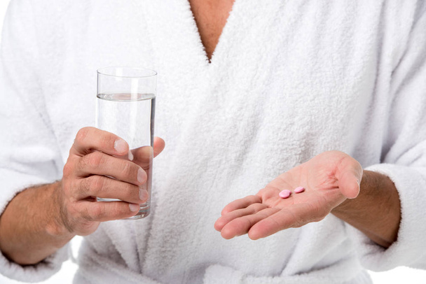 körülvágott kép felnőtt ember fürdőköpeny tabletták és pohár vizet elszigetelt fehér - Fotó, kép