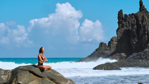 Vyrovnaná meditace jóga. Brunetka turistické žena přemýšlí v lotosové pozici na ostrohu nad malebným Praia da Marinha. Meditující žena na útesy z Kanárských ostrovů - Záběry, video