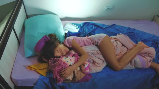 Urocza dziewczynka spać na rozkładanej i przytulić jej lalka baby. brunetka dziewczynka spanie w nocy w łóżku ukochaną z dzieciństwa. dzieci sen styl życia koncepcja - Materiał filmowy, wideo