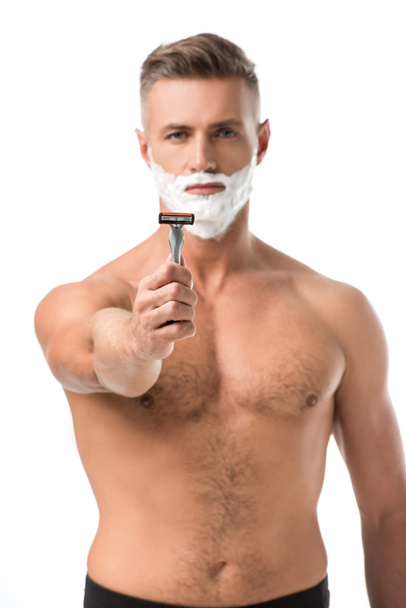 Selektiver Fokus muskulöser, hemdloser Mann mit Rasierschaum im Gesicht, der Rasiermesser isoliert auf Weiß zeigt - Foto, Bild