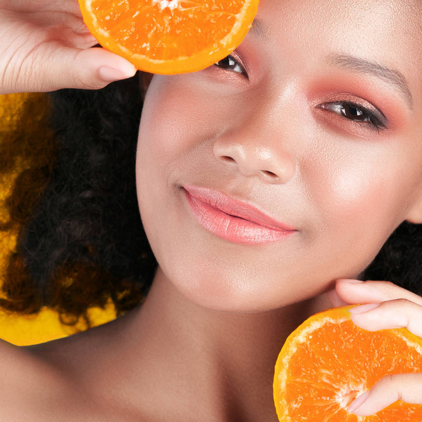 Young smiling black girl with clean perfect skin with orange close-up. Beauty portrait - Фото, зображення
