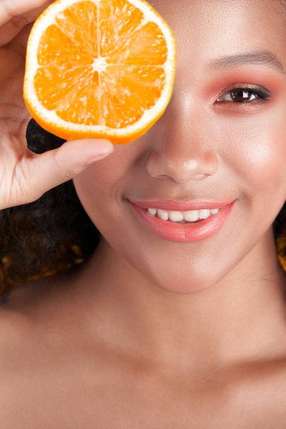 Young smiling black girl with clean perfect skin with orange close-up. Beauty portrait - Фото, зображення