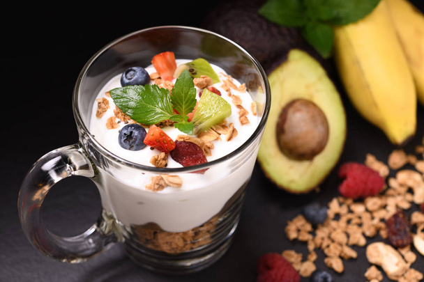 Close up yogurt with granola and fruits in glass on black granite stone table - Valokuva, kuva