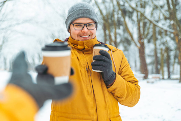 男は、雪が降った都市公園における友人にコーヒーを持ってくる。冬のシーズン - 写真・画像