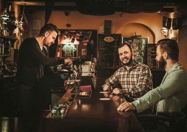 Viejos amigos divirtiéndose y bebiendo cerveza de barril en el bar
. - Foto, Imagen