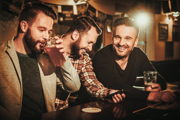 Vanhat ystävät hauskaa ja juominen luonnos olutta baaritiskillä pubissa
. - Valokuva, kuva