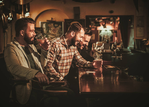 De vieux amis s'amusent et boivent de la bière pression au comptoir du bar au pub
. - Photo, image
