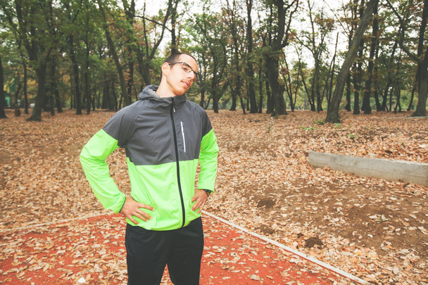 Fitness young man workout at park in autumn morning. Healthy man doing warm up exercise before training. - Photo, Image