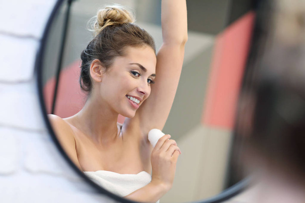 Молодая женщина использует дезодорант в ванной комнате
 - Фото, изображение
