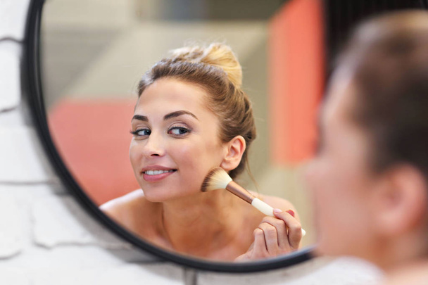 Mulher jovem aplicando maquiagem com escova no banheiro
 - Foto, Imagem