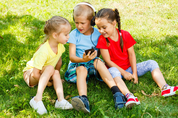 Η εταιρεία τα παιδιά που κάθεται στο γρασίδι με smartphone στο πάρκο  - Φωτογραφία, εικόνα