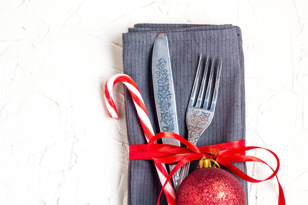Ajuste de mesa de Navidad con cuchillo, tenedor, bola roja, bastón de caramelo y cinta sobre mesa blanca con copyspace
. - Foto, imagen