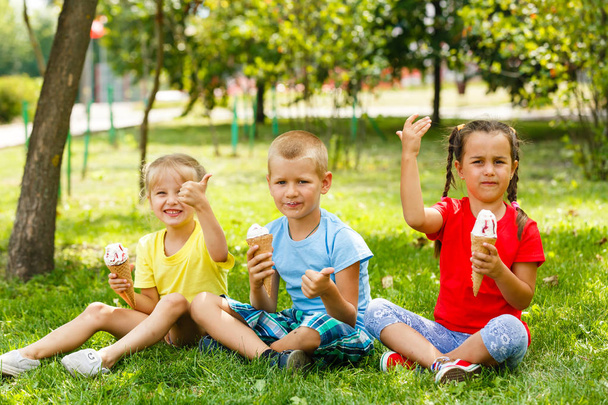 Маленькі діти сидять на зеленій траві і їдять морозиво
  - Фото, зображення