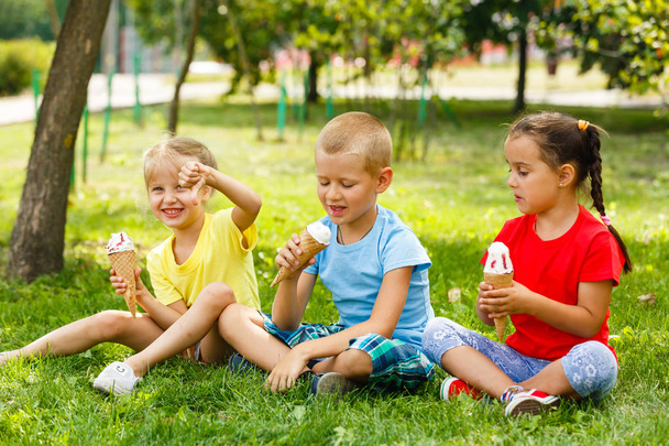 小さな子供緑の草の上に座って、アイスクリームを食べる  - 写真・画像