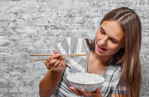 portrait of young teenager brunette girl with long hair eating rice on gray wall background - Foto, Imagem