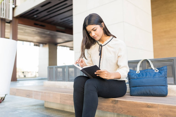 Young professional reading book while sitting by purse - Photo, Image