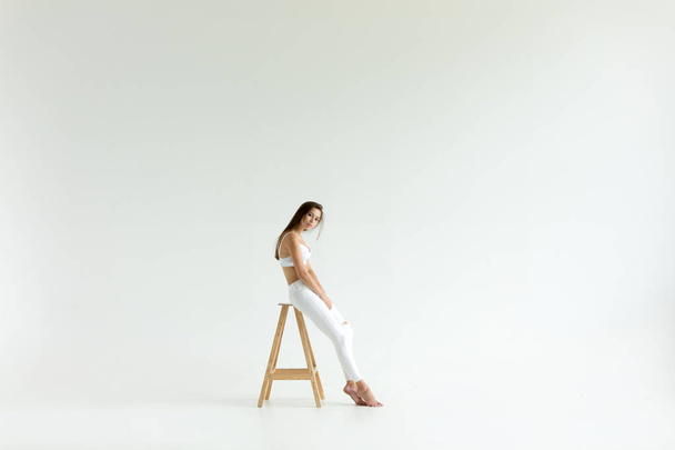 Attractive young woman in white bra and jeans sits on white background. - Fotó, kép