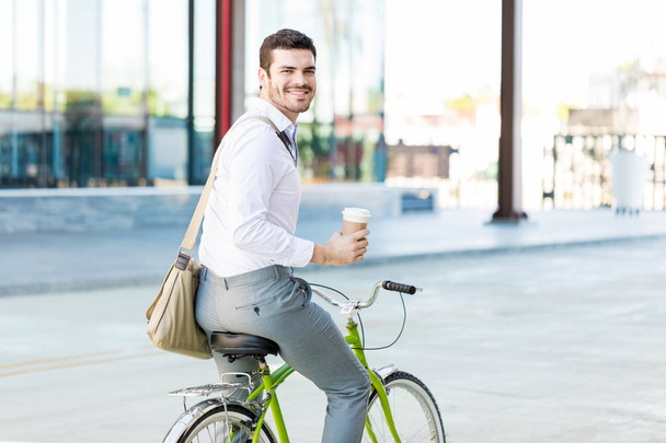 Ritratto di amministratore sorridente mentre tiene in mano la tazza usa e getta e va in bicicletta in città
 - Foto, immagini