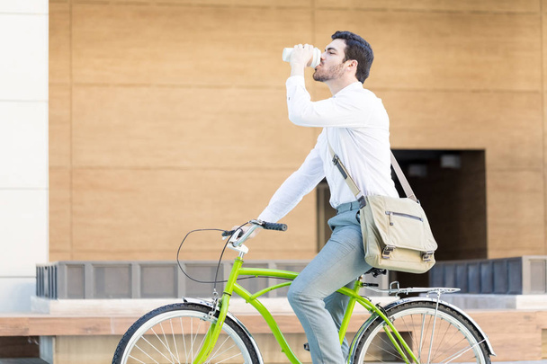 Side näkymä houkutteleva miespuolinen johtaja saada virkistää ajaa polkupyörällä vastaan toimistorakennus
 - Valokuva, kuva