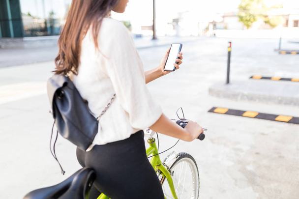 Sección media de una profesional hispana que usa GPS mientras monta en bicicleta en la calle
 - Foto, imagen