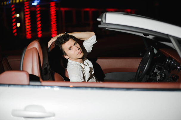 Portrait of a handsome man in white cabriolet. Nightlife. Businessman in suit in luxury car - Foto, afbeelding