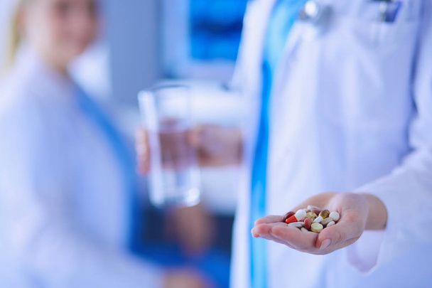 prise de vue du médecin tenant des pilules et un verre d'eau à la clinique avec un collègue sur le fond. - Photo, image