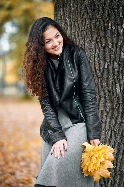 Woman with yellow leaves stand near big tree in autumn city park. - Foto, Bild