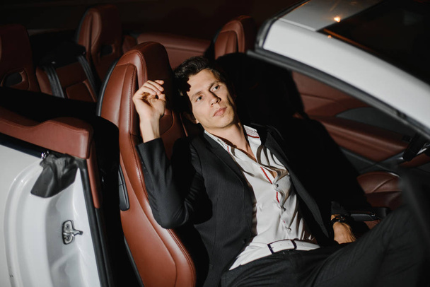 Portrait of a handsome man in white cabriolet. Nightlife. Businessman in suit in luxury car. - Fotó, kép
