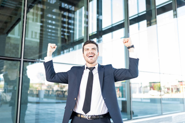 Cheerful Hispanic businessman raising arms and celebrating victory outside office building - Fotografie, Obrázek