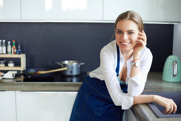 Portrait of young woman standing with arms crossed against kitchen background - 写真・画像