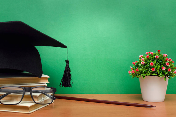 Stack of books, glasses and graduation cap on green school board background. Back to school. - 写真・画像