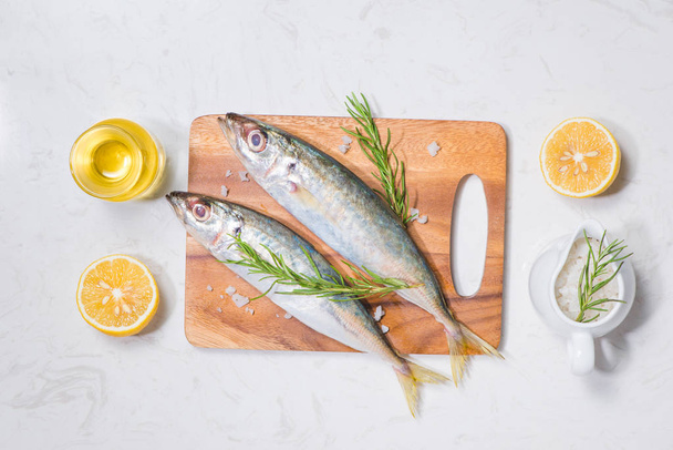 Plat de poisson cuisson avec divers ingrédients. Poisson cru frais décoré de tranches de citron et d'herbes sur fond gris
 - Photo, image