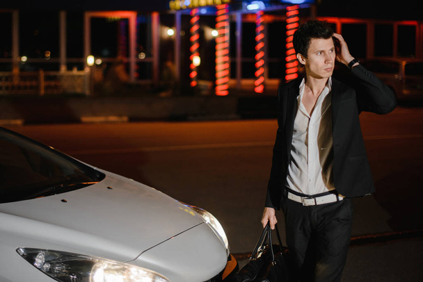 Portrait of a handsome man standing next to his white cabriolet. Nightlife. Businessman in suit in luxury car - Fotó, kép