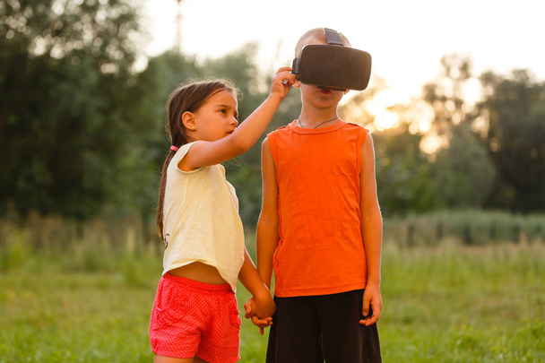 little girl with brother in virtual reality headsets playing together in park - Photo, Image