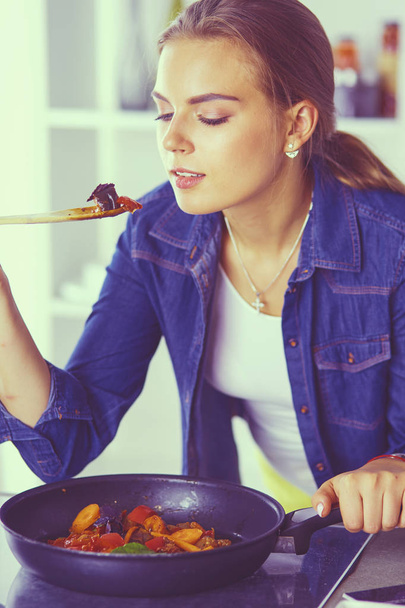 Νεαρή γυναίκα μαγειρεύει υγιεινό φαγητό κρατώντας ένα τηγάνι με λαχανικά είναι αυτό. Υγιεινός τρόπος ζωής, μαγειρική στο σπίτι έννοια - Φωτογραφία, εικόνα