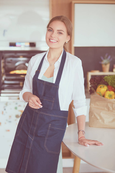 Portrait of young woman standing with arms crossed against kitchen background. - Photo, Image