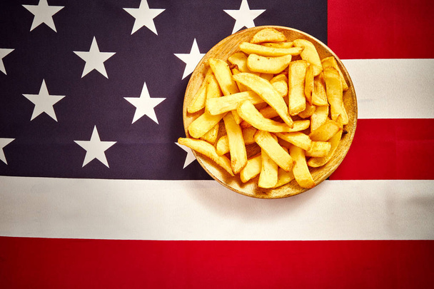 vista superior de deliciosas batatas fritas em uma placa de madeira no fundo da bandeira dos EUA
 - Foto, Imagem