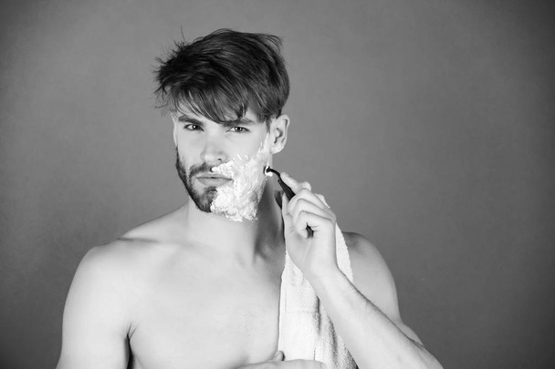 Handsome macho with naked chest shaving beard with safety razor - 写真・画像