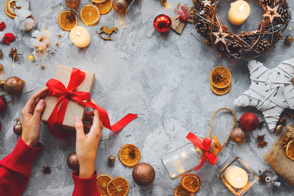  Χριστουγεννιάτικο φόντο με διακοσμήσεις και γυναικεία χέρια, κιβώτιο δώρων, κεριά, τα πορτοκάλια, κάρδαμο, μπάλες. Επίπεδη θέσει. Χώρο αντίγραφο - Φωτογραφία, εικόνα