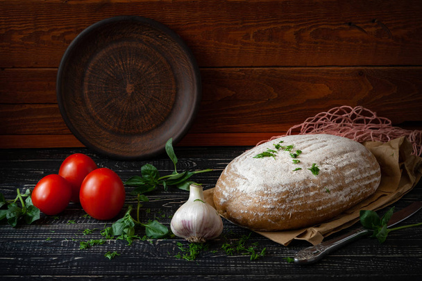 fresh baked bread with tomatoes and garlic with basil on a dark wooden background - Photo, image