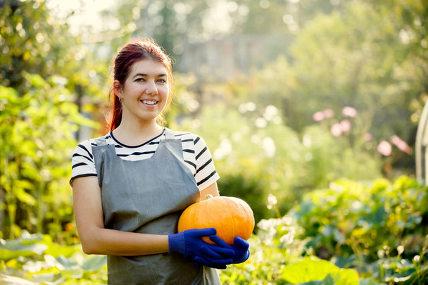Image of smiling girl with pumpkin in hands at garden - Photo, image