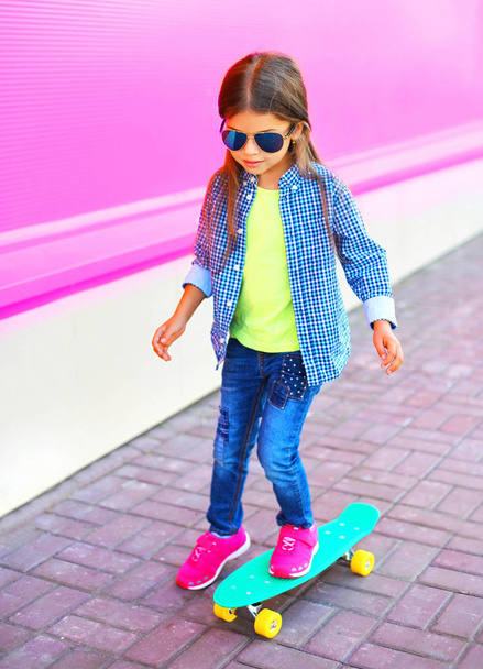 Fashion child little girl on skateboard on colorful pink wall background - Foto, Imagen