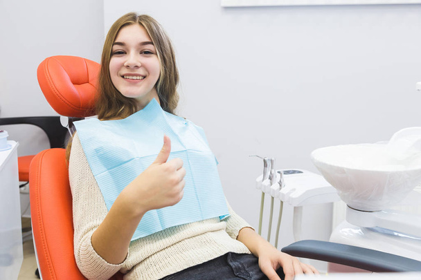 Dental clinic. Reception, examination of the patient. Teeth care. Young girl shows thumb up sign in dentist office - Foto, immagini